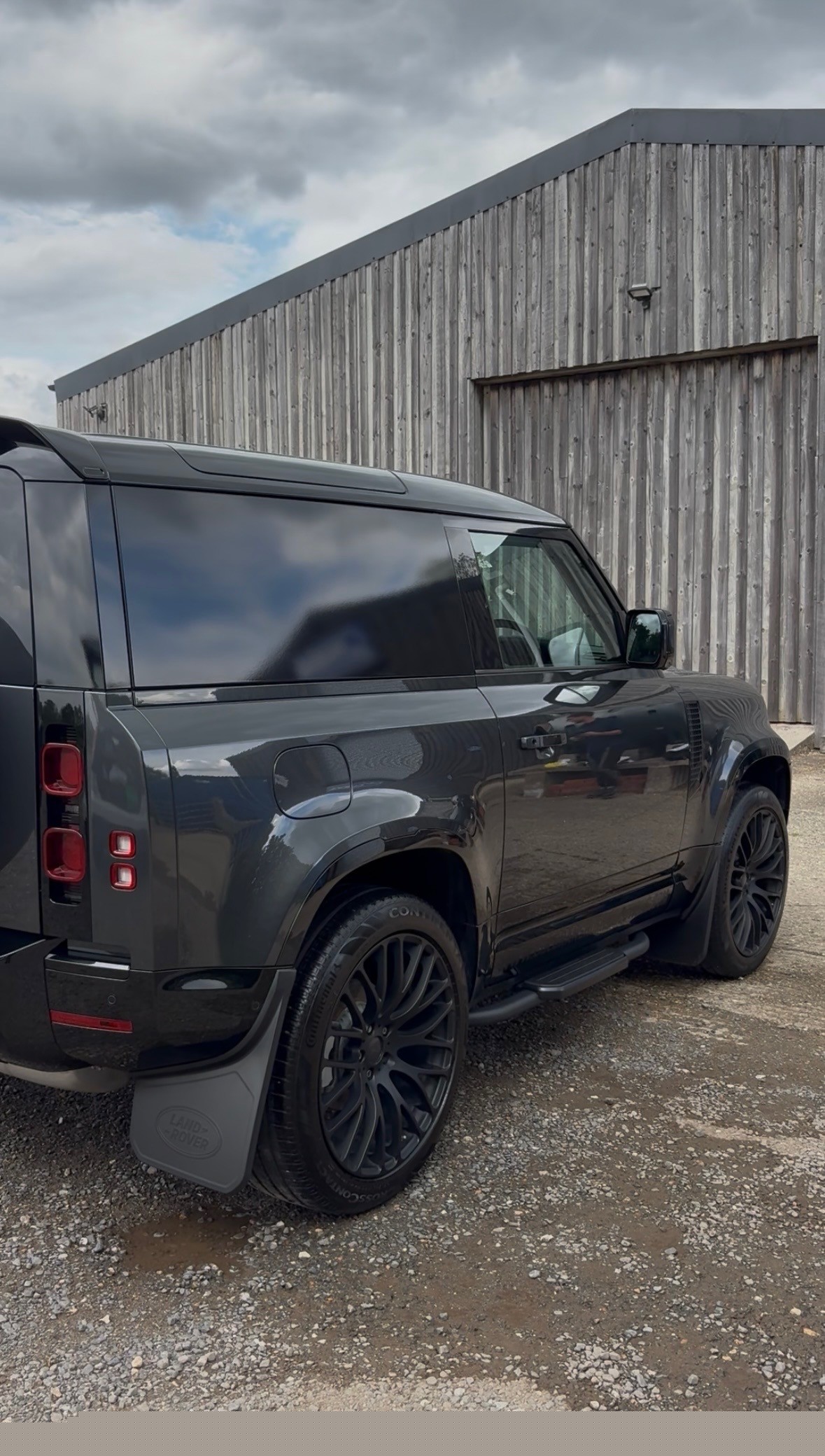 Dark Land Rover Defender — rear beside barn